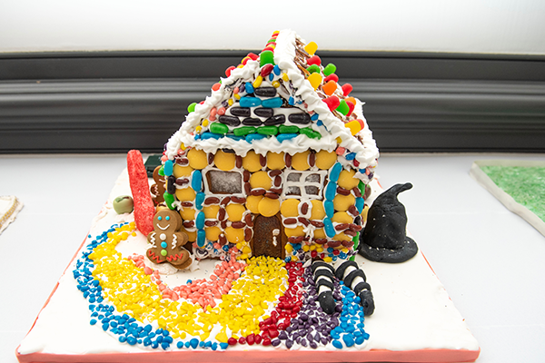 A heavily decorated gingerbread house, adorned with many different types of candies. The yellow brick road leading to the house points directly to the witches legs sticking out from underneath the house's foundation.