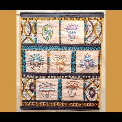 A quilted wall hanging featuring seven squares with different embroidered mask designs, surrounded by quilted strips of patterened fabric in shades of yellow and turqouise.