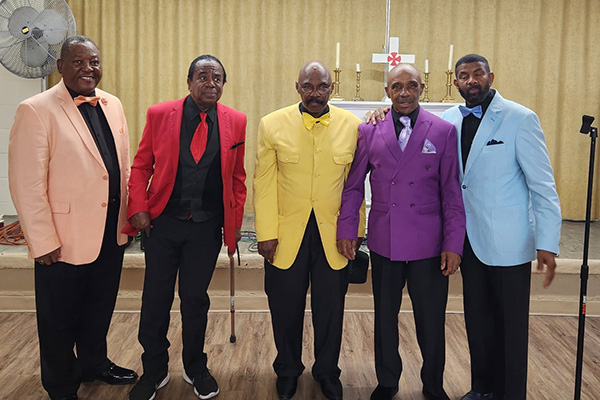 Five men in brightly-colored suit jackets pose in a room.