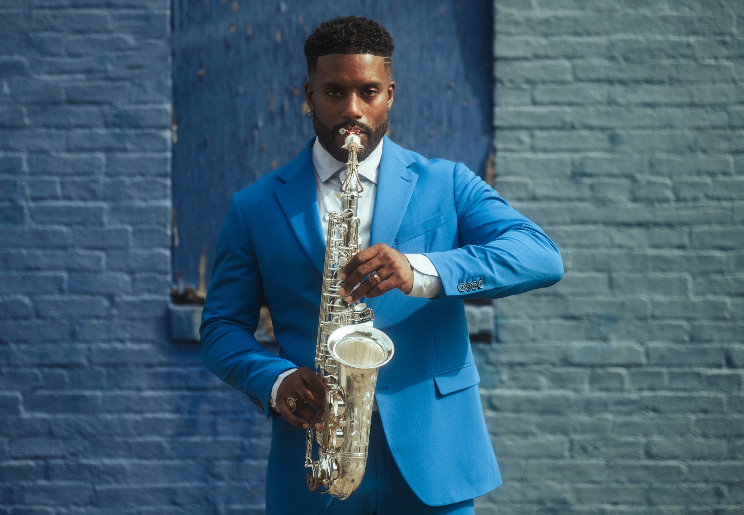Man in a blue suit playing a silver Alto Saxophone