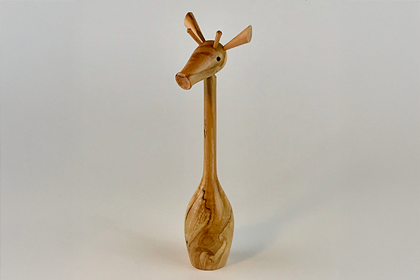 A wooden sculpture of a giraffe against a grey background.