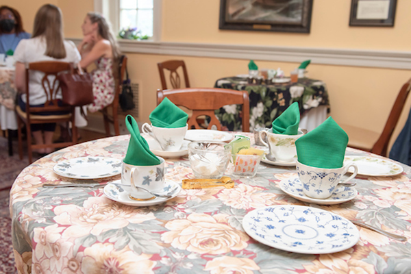 A table for four nicely decorated with plates and cups. there are green napkins folded and rising out of the tea cups.