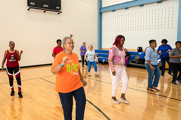 Nine seniors do aerobic exercise in a gymnasium.