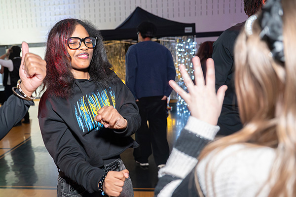 Several teens dance in a darkened gymnasium that is decorated with colorful lights.