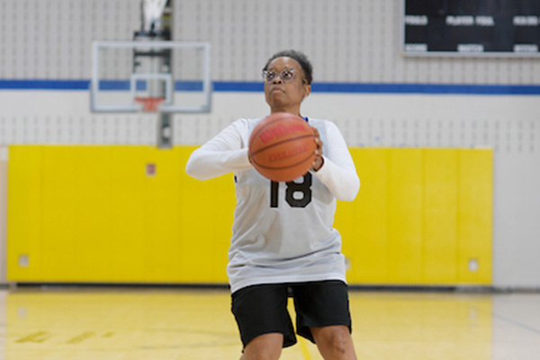 A senior plays basketball in a gymnasium.