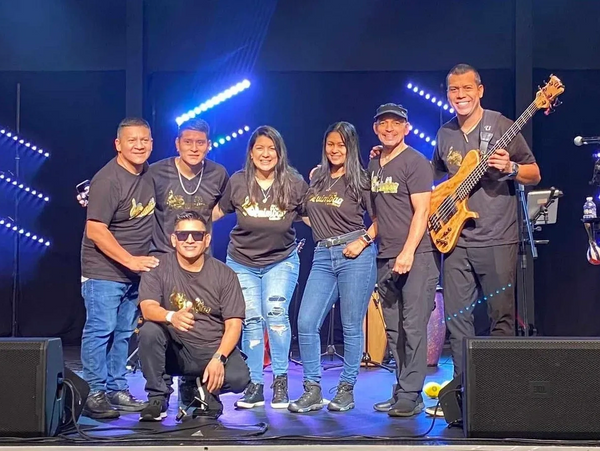 Community band members pose on stage with instruments under blue lights before a live performance.
