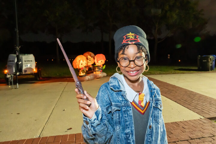A girl wearing a beanie hat holds a magical wand outdoors.